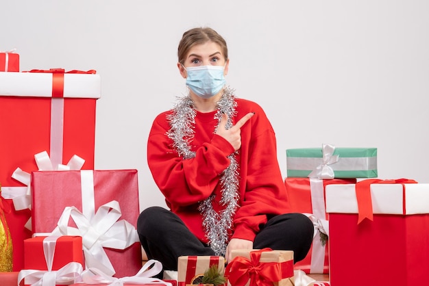 Vista frontal mujer joven sentada con regalos de Navidad en máscara estéril