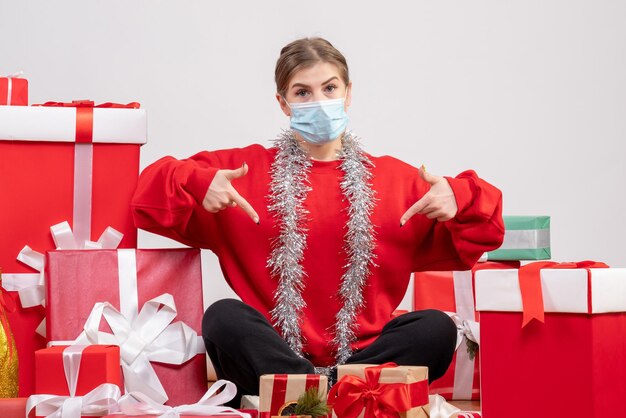 Vista frontal mujer joven sentada con regalos de Navidad en máscara estéril