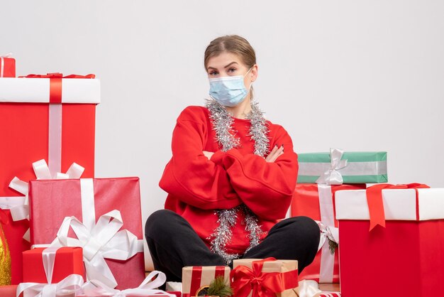 Vista frontal mujer joven sentada con regalos de Navidad en máscara