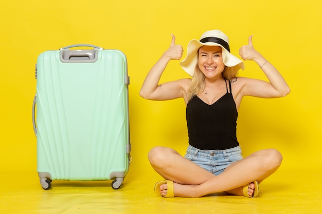 Foto gratuita vista frontal mujer joven sentada con su bolsa verde sintiéndose feliz en la pared amarilla viaje vacaciones sol viaje viaje niña