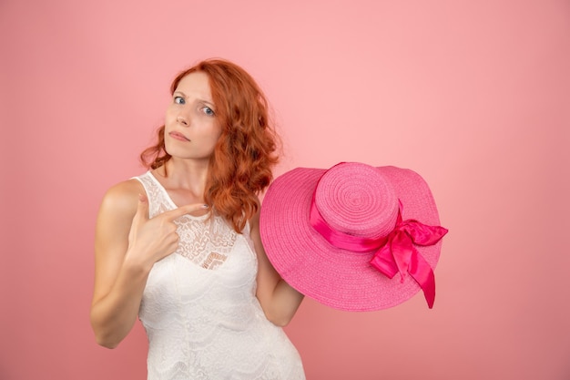 Vista frontal de la mujer joven con sombrero rosa en pared rosa