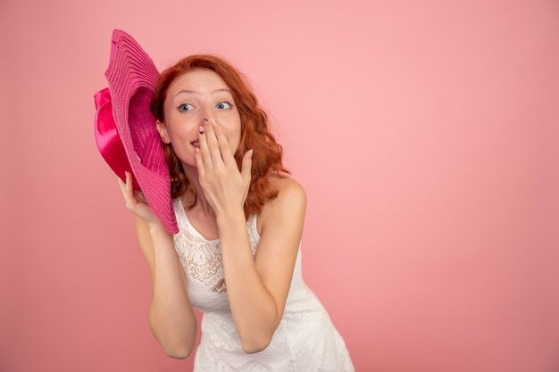 Vista frontal de la mujer joven con sombrero rosa en pared rosa