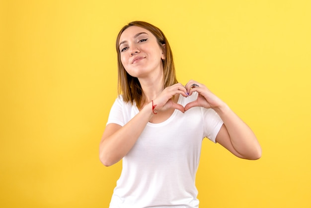 Vista frontal de la mujer joven sonriendo y enviando amor en la pared amarilla