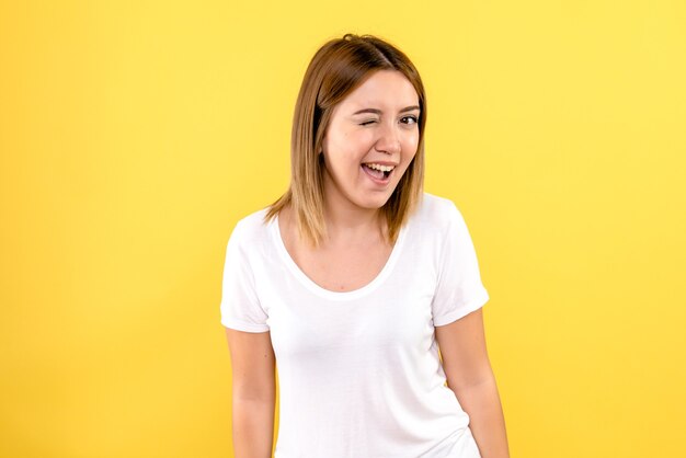 Vista frontal de la mujer joven sonriendo y guiñando un ojo en la pared amarilla