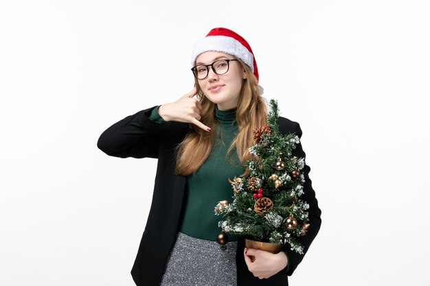 Vista frontal mujer joven sosteniendo árbol de vacaciones en la pared blanca juguete año nuevo navidad