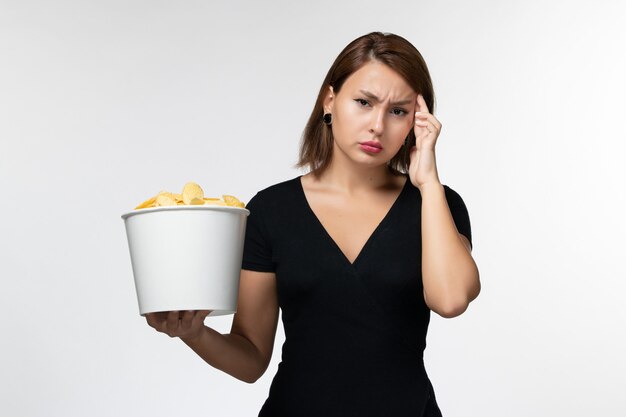 Foto gratuita vista frontal mujer joven sosteniendo la cesta con papas fritas y pensando profundamente en la superficie blanca