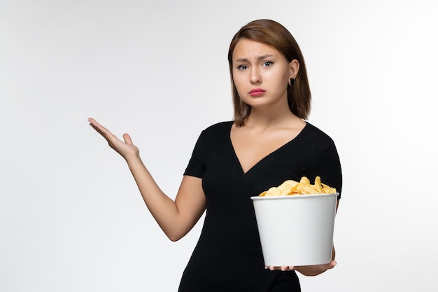 Vista frontal mujer joven sosteniendo la cesta con papas fritas viendo la película sobre una superficie blanca