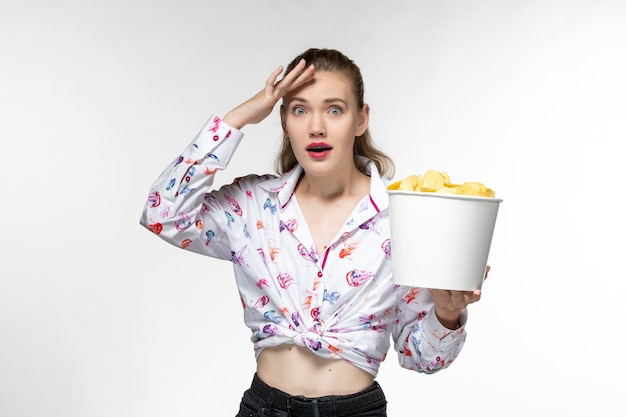 Foto gratuita vista frontal mujer joven sosteniendo la cesta con papas fritas viendo la película en la superficie blanca clara