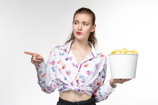 Foto gratuita vista frontal mujer joven sosteniendo la cesta con patatas fritas y mirando a su alrededor sobre una superficie blanca