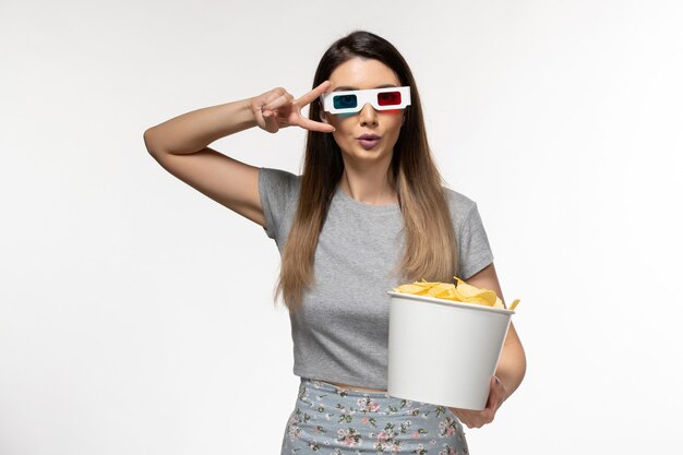 Vista frontal mujer joven sosteniendo chips mientras ve la película en gafas de sol d sobre superficie blanca clara