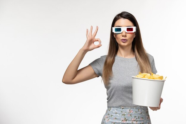 Vista frontal mujer joven sosteniendo chips mientras ve la película en gafas de sol d sobre superficie blanca