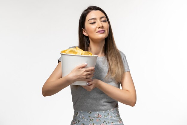 Vista frontal mujer joven sosteniendo chips mientras ve la película en la superficie blanca clara