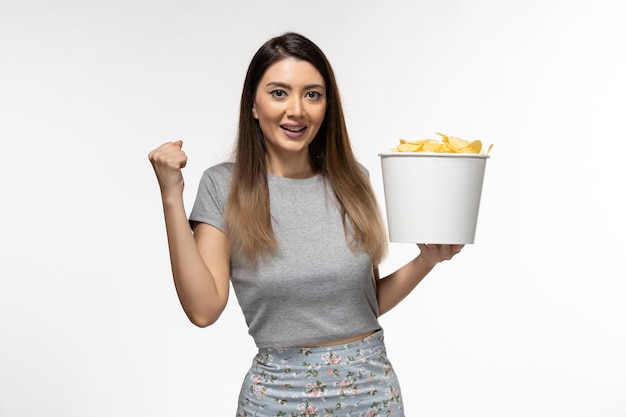 Vista frontal mujer joven sosteniendo chips mientras ve la película en la superficie blanca clara