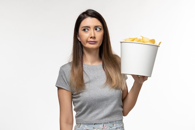 Vista frontal mujer joven sosteniendo chips mientras ve la película en la superficie blanca clara