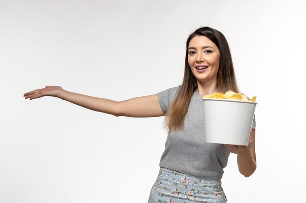 Vista frontal mujer joven sosteniendo chips mientras ve la película en la superficie blanca clara