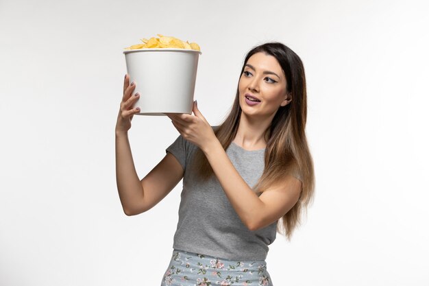 Vista frontal mujer joven sosteniendo chips y viendo películas en la superficie blanca clara