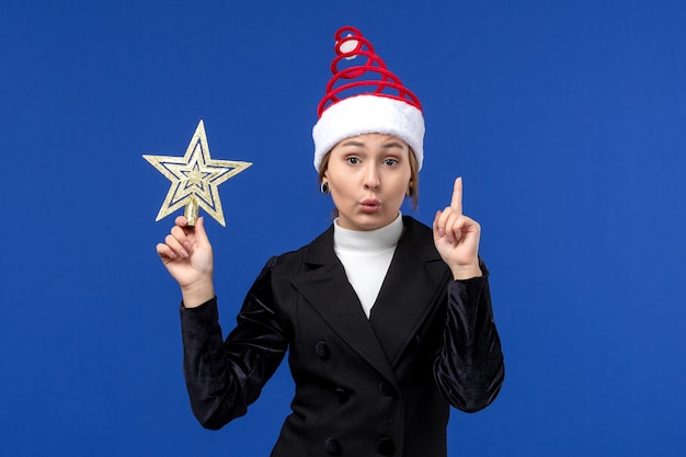 Vista frontal mujer joven sosteniendo una decoración en forma de estrella en el escritorio azul mujer de vacaciones de año nuevo