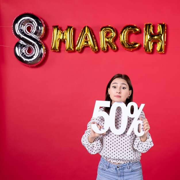 Vista frontal mujer joven sosteniendo la escritura en marzo decorado fondo rojo compras igualdad cariñosa moda mujer centro comercial vacaciones