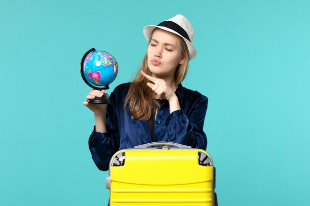 Vista frontal mujer joven sosteniendo el globo y preparándose para las vacaciones sobre fondo azul claro viaje femenino viaje vacaciones en avión de mar