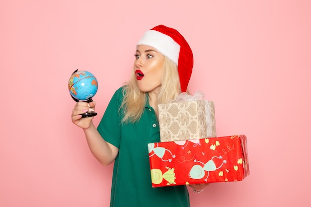 Foto gratuita vista frontal mujer joven sosteniendo globo y regalos de navidad en la pared rosa modelo fotográfico mujer navidad año nuevo color vacaciones