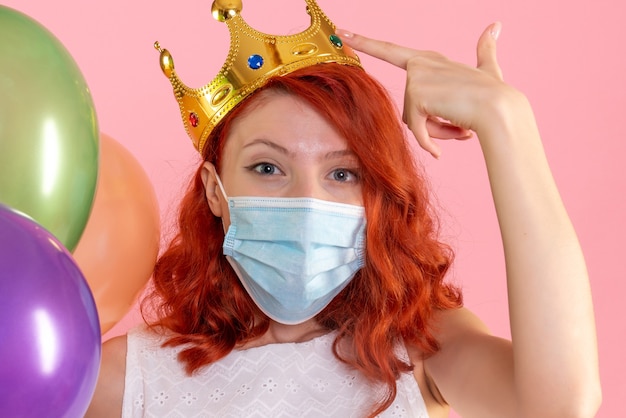 Foto gratuita vista frontal de la mujer joven sosteniendo globos de colores en máscara estéril en la pared rosa