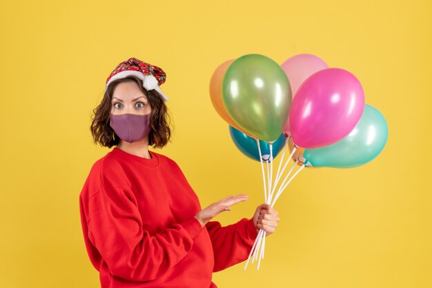 Vista frontal mujer joven sosteniendo globos en máscara estéril en amarillo