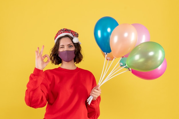 Vista frontal mujer joven sosteniendo globos en máscara estéril en amarillo