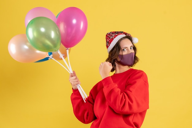 Vista frontal mujer joven sosteniendo globos en máscara estéril en amarillo