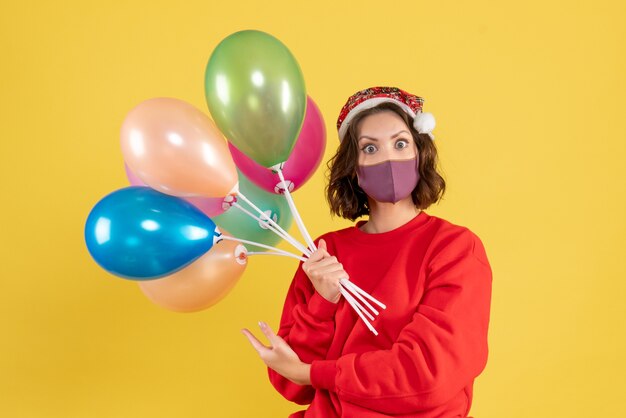 Vista frontal mujer joven sosteniendo globos en máscara estéril en amarillo