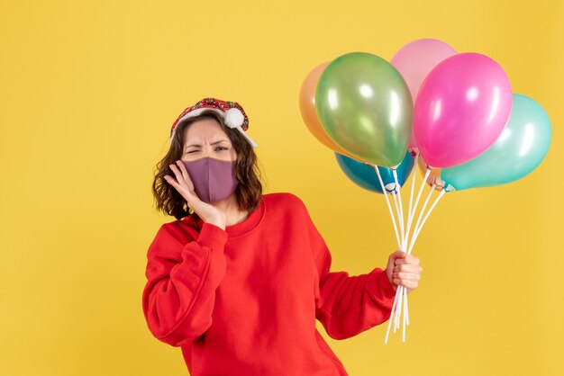 Vista frontal mujer joven sosteniendo globos en máscara estéril en amarillo