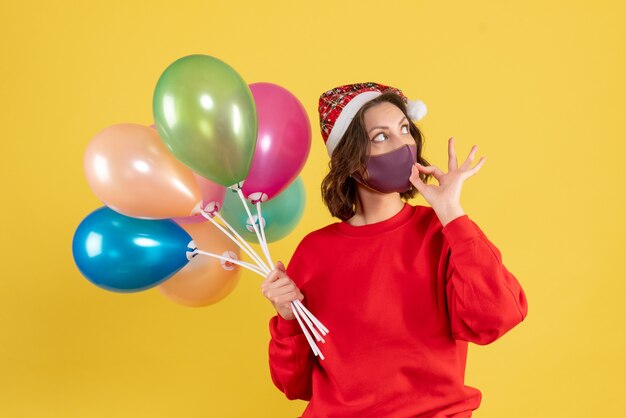 Vista frontal mujer joven sosteniendo globos en máscara estéril en amarillo