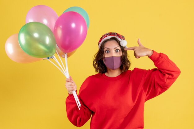 Vista frontal mujer joven sosteniendo globos en máscara estéril en amarillo