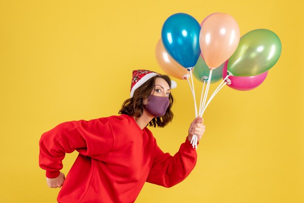 Vista frontal mujer joven sosteniendo globos en máscara estéril en amarillo