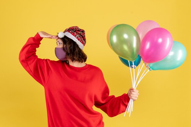 Vista frontal mujer joven sosteniendo globos en máscara estéril en amarillo