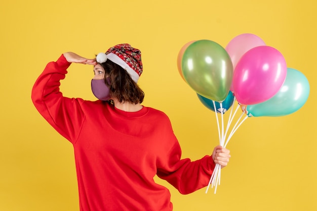 Vista frontal mujer joven sosteniendo globos en máscara estéril en amarillo