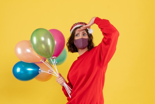 Vista frontal mujer joven sosteniendo globos en máscara estéril en amarillo