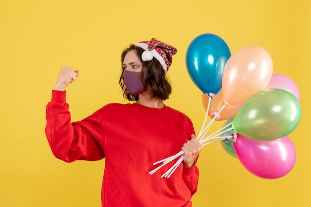 Foto gratuita vista frontal mujer joven sosteniendo globos en máscara estéril en amarillo