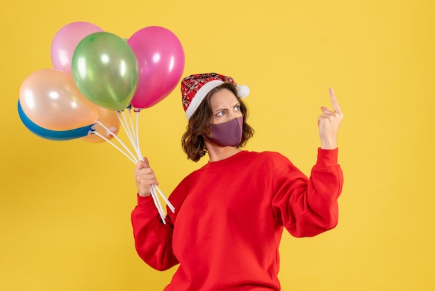 Vista frontal mujer joven sosteniendo globos en máscara estéril en amarillo