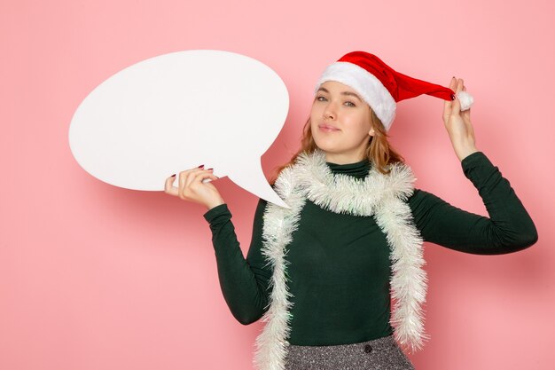 Vista frontal mujer joven sosteniendo un gran cartel blanco y sonriendo en la pared rosa Navidad año nuevo modelo vacaciones color emoción