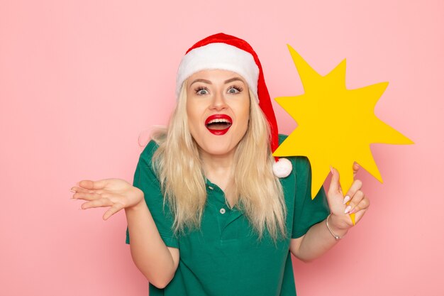 Vista frontal mujer joven sosteniendo gran figura amarilla en la pared rosa modelo mujer foto de vacaciones de navidad año nuevo color