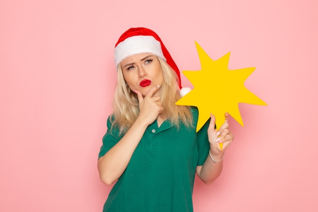 Vista frontal mujer joven sosteniendo gran figura amarilla en la pared rosa modelo mujer foto de vacaciones de navidad año nuevo color