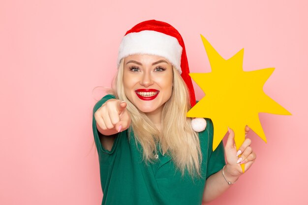 Vista frontal mujer joven sosteniendo gran figura amarilla en la pared rosa modelo mujer foto de vacaciones de navidad año nuevo color