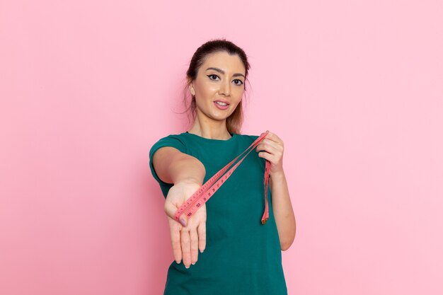 Vista frontal mujer joven sosteniendo la medida de la cintura en la pared de color rosa claro ejercicios deportivos de belleza atleta entrenamientos delgado