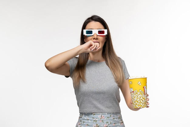 Vista frontal mujer joven sosteniendo palomitas de maíz y viendo películas en gafas de sol d sobre superficie blanca