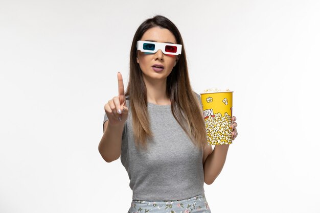 Vista frontal mujer joven sosteniendo palomitas de maíz y viendo películas en gafas de sol d sobre superficie blanca