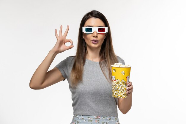 Vista frontal mujer joven sosteniendo palomitas de maíz y viendo películas en gafas de sol d sobre superficie blanca