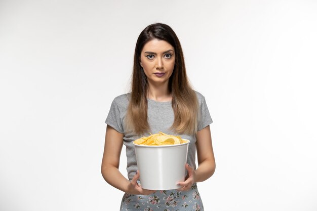 Vista frontal mujer joven sosteniendo papas fritas mientras ve la película en la superficie blanca