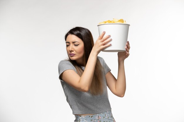 Vista frontal mujer joven sosteniendo papas fritas mientras ve la película en la superficie blanca