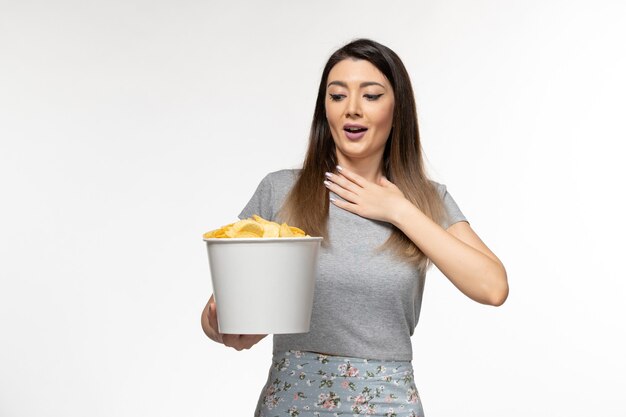 Vista frontal mujer joven sosteniendo papas fritas mientras ve una película en la superficie de color blanco claro