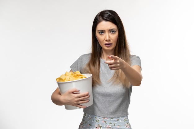 Vista frontal mujer joven sosteniendo papas fritas mientras ve una película en la superficie de color blanco claro